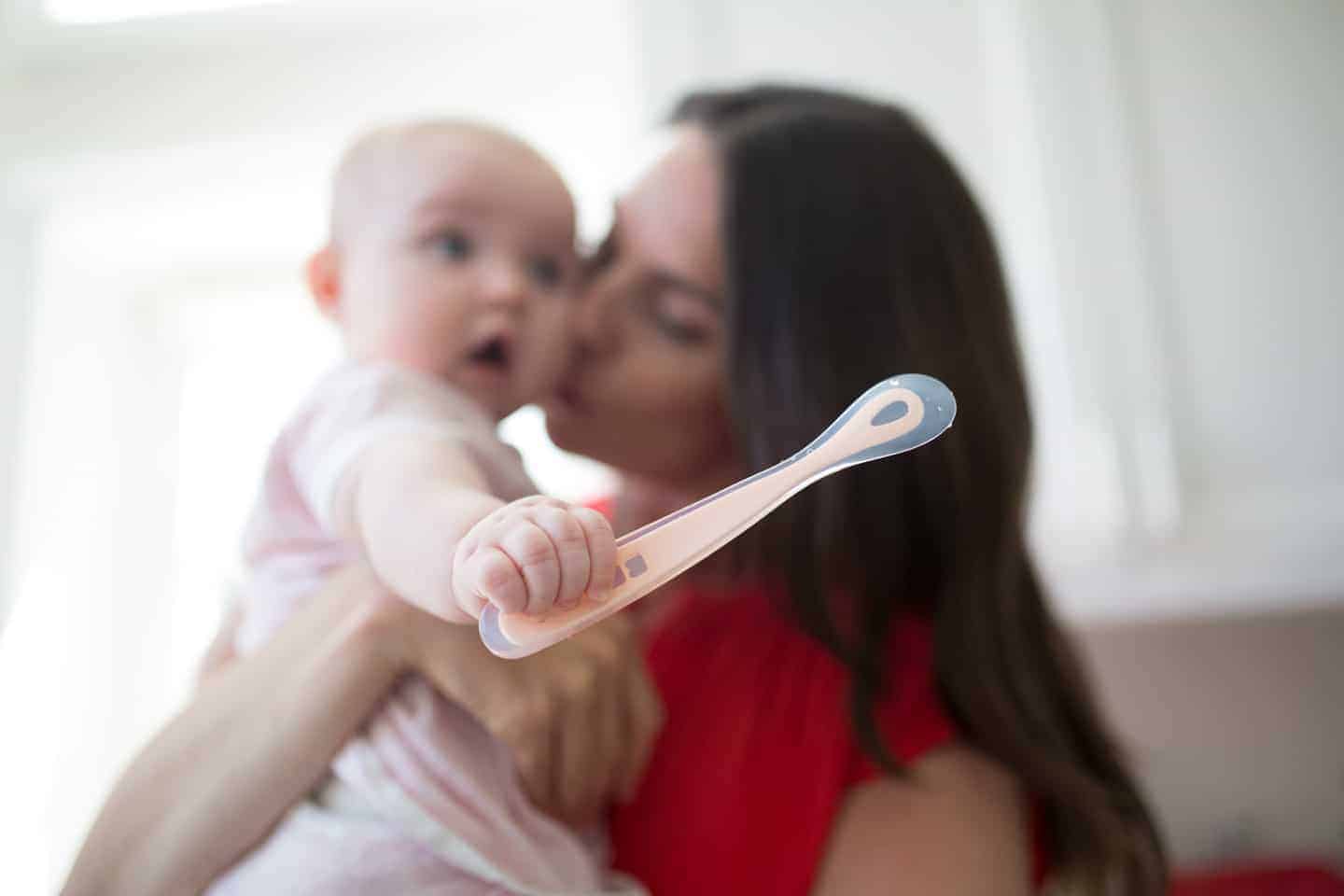 Mom Holding Her Baby Who Is Holding First Foods Silicone Spoon Rose