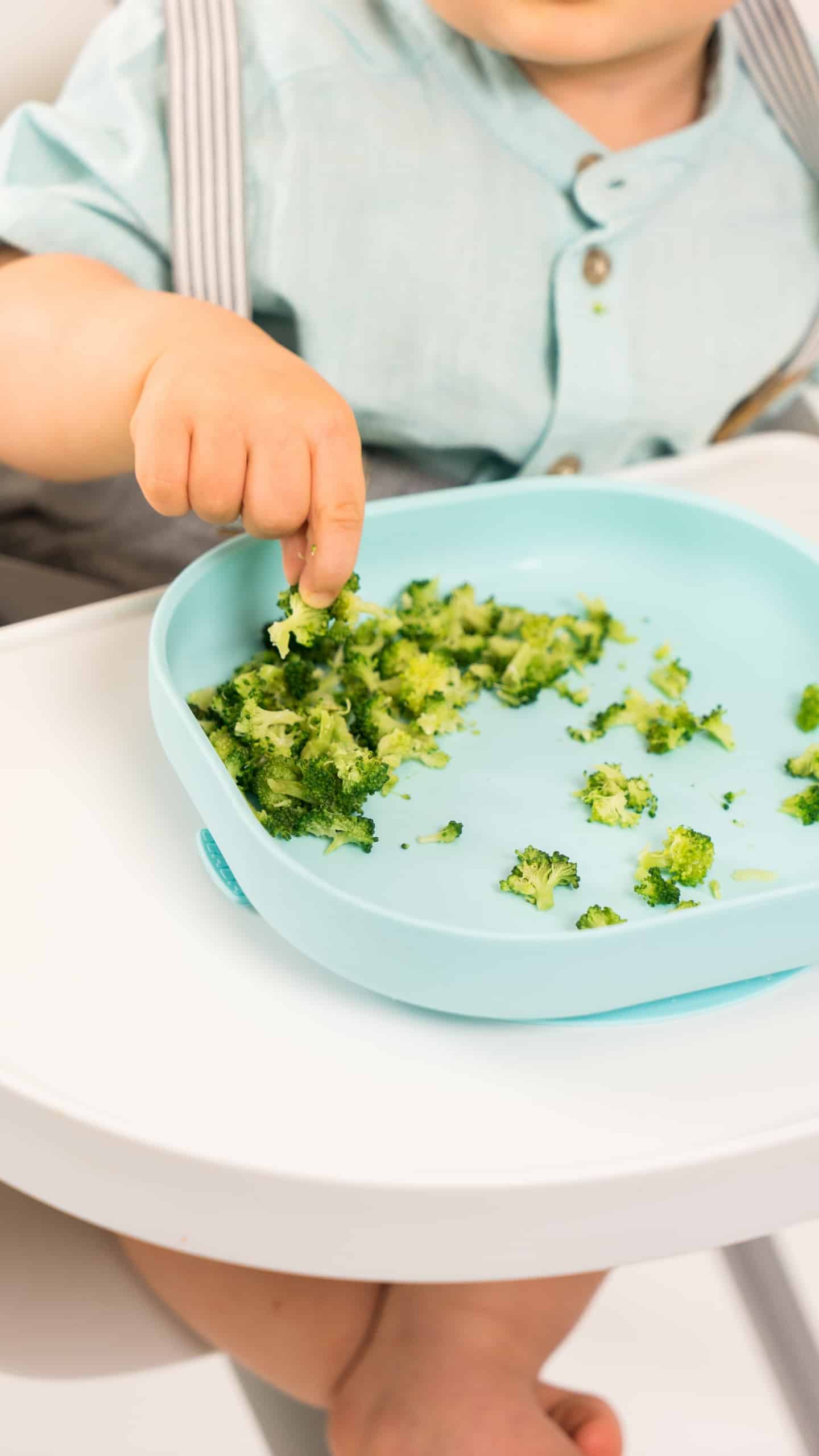 toddler hand picking broccoli from silicone suction meal set pastel