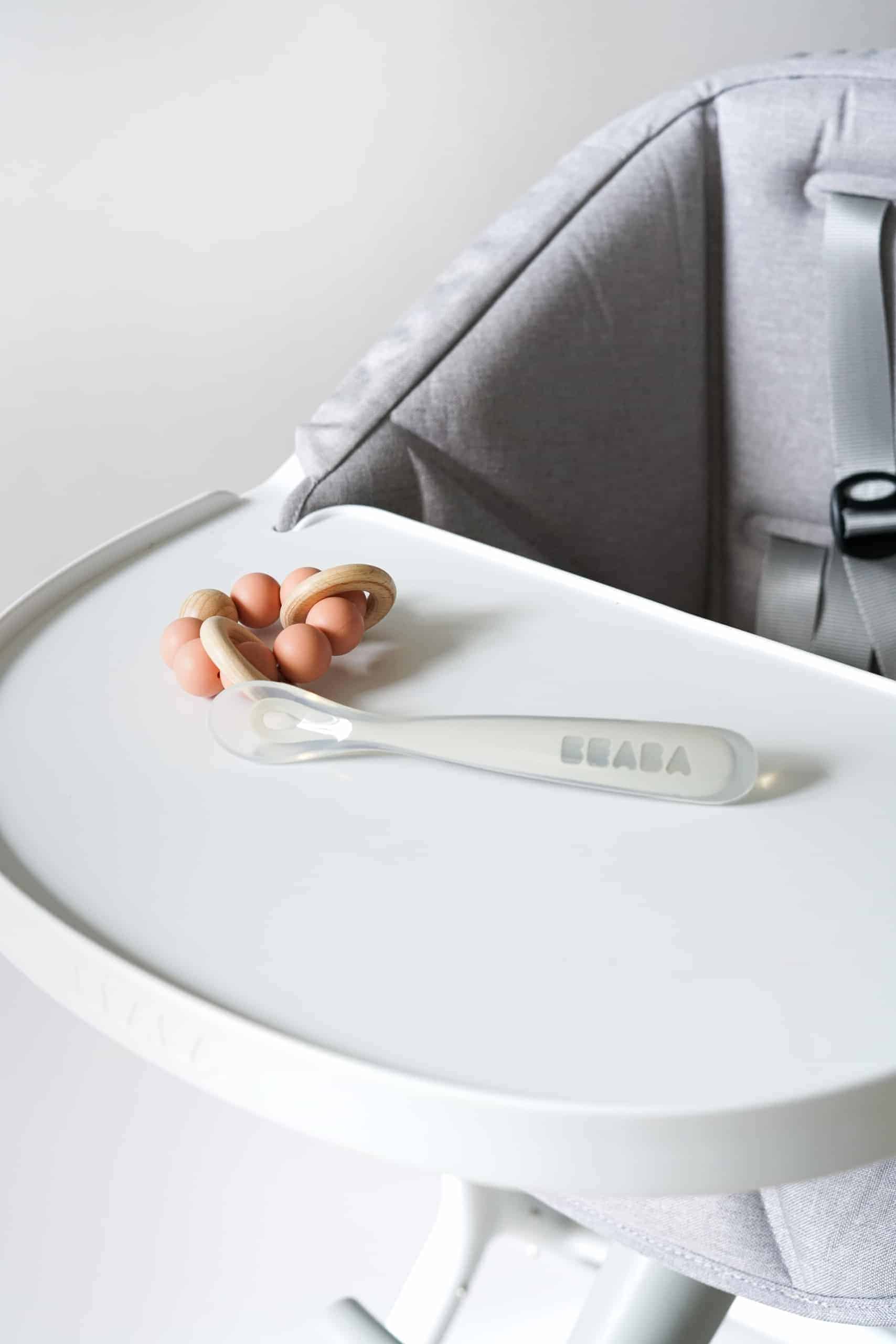 Beaba first foods spoon on high chair tray next to rattle