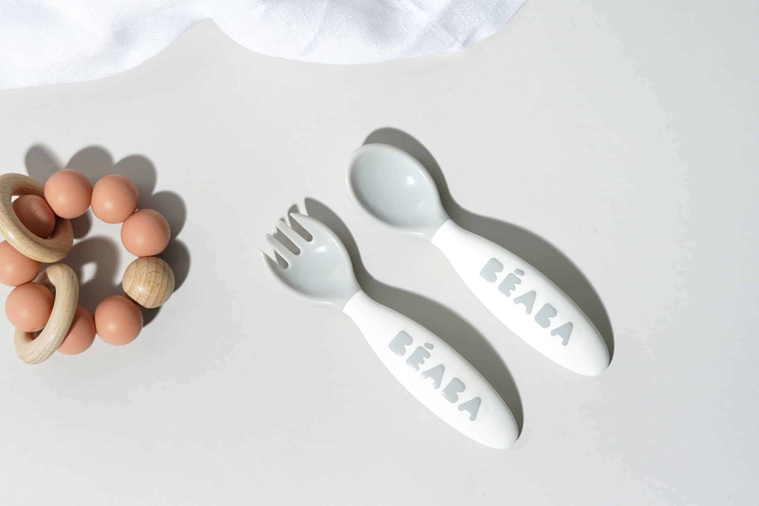 Beaba Toddler cutlery in cloud next to baby rattle