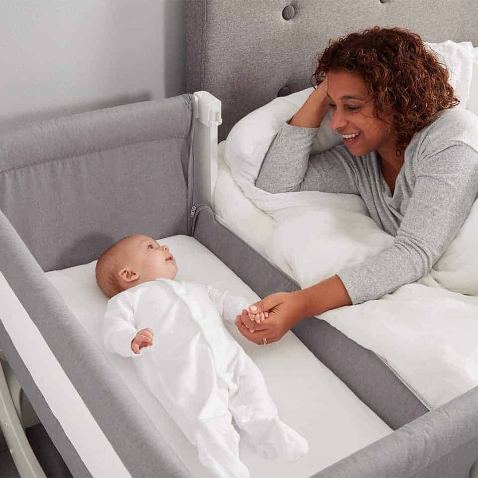Mom holding baby's hand in Beaba by Shnuggle Air Bedside Crib