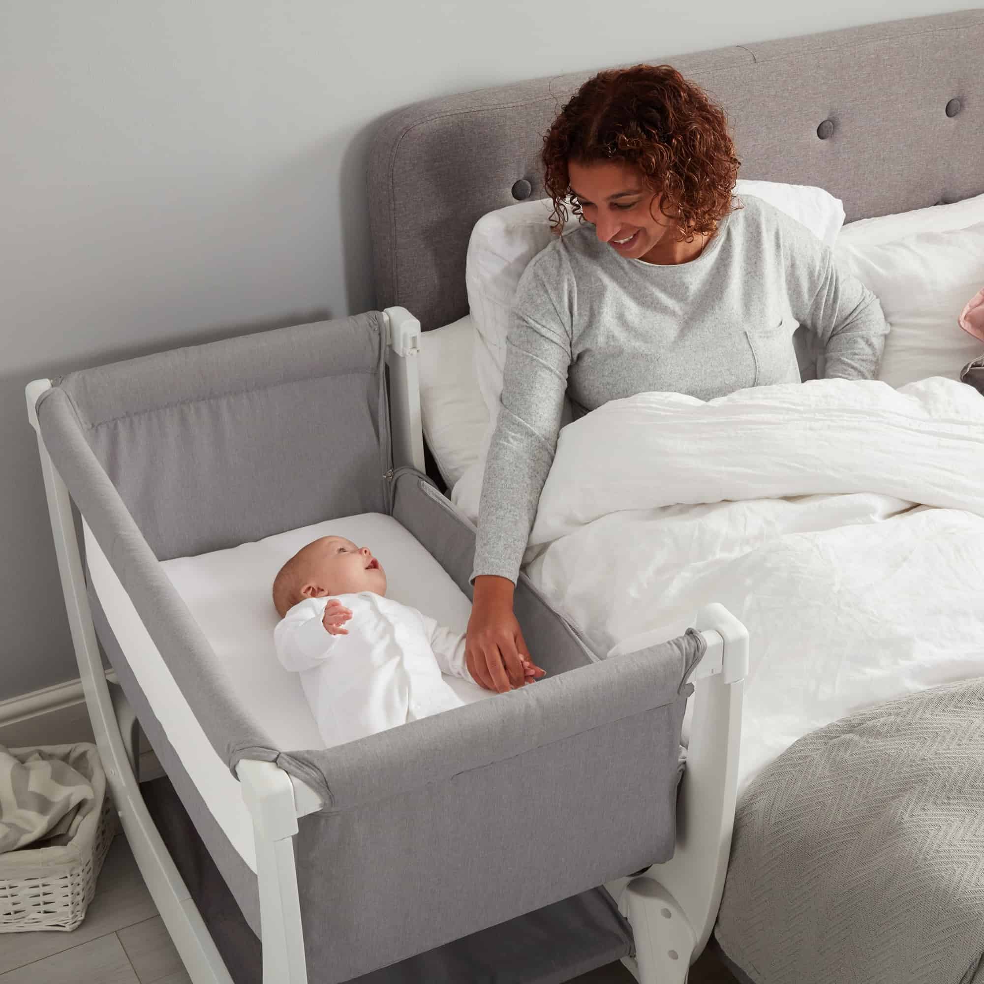 mom holding baby's hand in bedside bassinet
