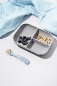 Beaba Divided Suction Plate and spoon with cheerios and blueberry in it. Next to table linen